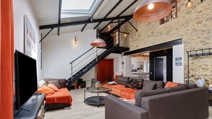 A spacious living area with a sofa, a coffee table, and a TV. A staircase leads to an upper level. - Gîte La Ferme Du Mesnil with Private Terrace, Wi-Fi, and Air Conditioning (Sèvremont)