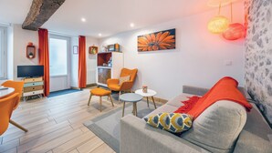 Een moderne woonkamer met een bank, stoelen, een salontafel, een televisie en een keuken in de achtergrond.