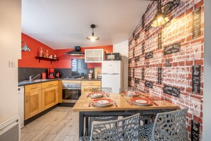 A compact kitchen with a dining area, featuring a brick wall, modern appliances, and a unique table setting. - Holiday Home 'Le Clemenceau' with Wi-Fi (Les epesses)