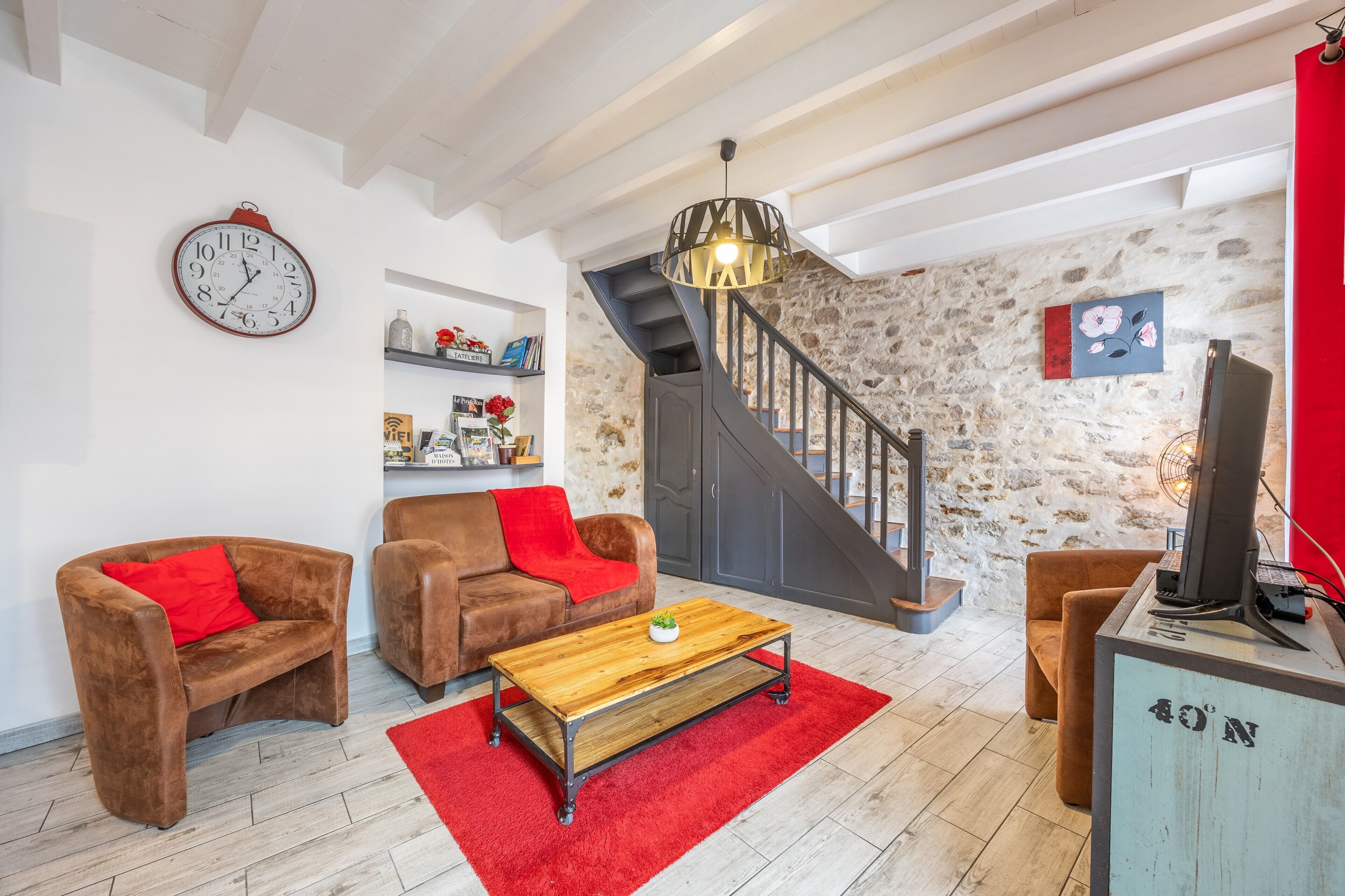 A living room with a staircase, a red sofa, a wooden coffee table, and a TV on a stand.