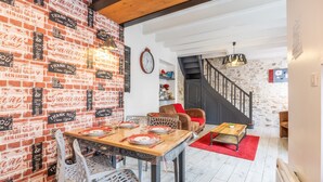Een eetgedeelte met een bakstenen muur, een houten tafel gedekt voor twee personen, en een trap die naar een hoger niveau leidt.