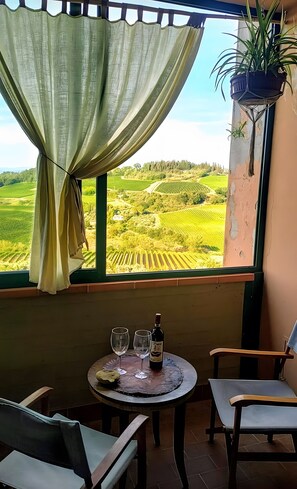 Un balcone con vista sui vigneti, un tavolo con bicchieri da vino e una bottiglia, e una sedia.