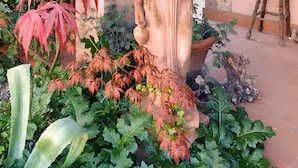 A statue in a garden with red foliage, a wooden table, and a rustic backdrop. - Casa Bice Room with Private Terrace and Wi-Fi (Marcialla)
