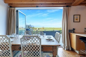 Comedor con mesa preparada para cuatro, techo de madera y vista a un campo verde a través de amplias ventanas.