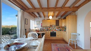 Un comedor con una mesa lista para cuatro personas, una cocina con armarios de madera y salpicadero colorido, y vistas a zonas verdes.