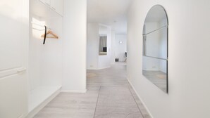 Ein Flur mit weißen Wänden, Holzboden und einem großen Spiegel rechts.