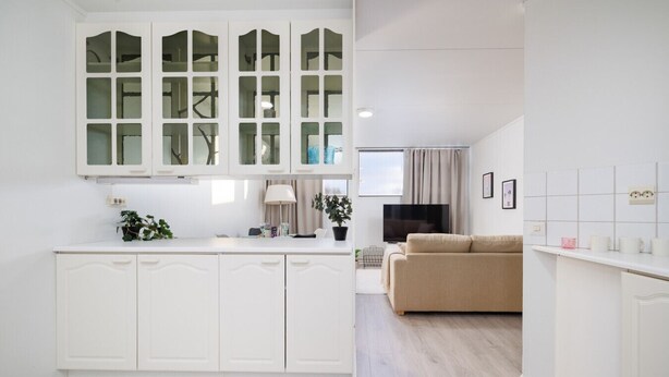 Eine moderne Küche mit weißen Schränken und einer zentralen Kochinsel, ein beiges Sofa in einem Wohnbereich und ein Flachbildfernseher.