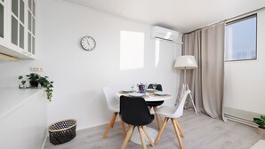 Ein moderner, hell erleuchteter Essbereich mit einem runden Tisch, weißen Stühlen und einer Uhr an der Wand.