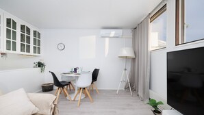 Ein modernes Wohnzimmer mit einer Couch, einem Esstisch mit Stühlen, einem Fernseher und einer Lampe.