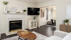 A living room with a fireplace, a flat-screen TV mounted on the wall, a dining area with a table and chairs, and a hallway leading to another room. - Family Gem in Pelham 3BR/2Bath 1 LEVEL Pet friendly home (Pelham)
