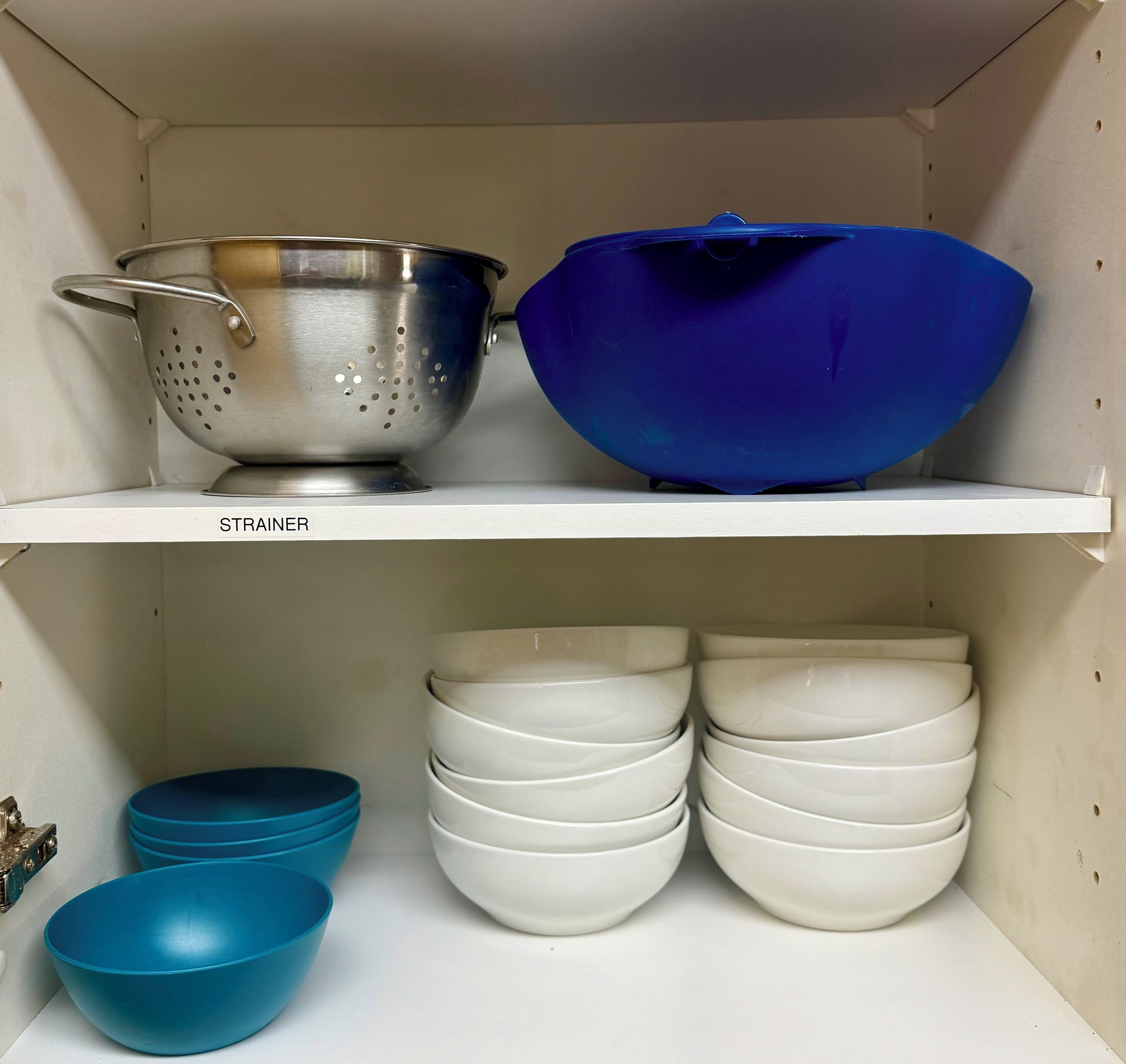 A kitchen shelf with a colander, a blue mixing bowl, and stacked white bowls.