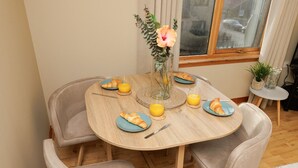 Een ronde houten eettafel met vier stoelen, een vaas met bloemen en borden met croissants en jus d'orange.