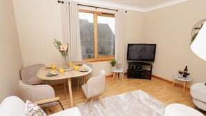 Een gezellige woonkamer met een eethoek, een flatscreen televisie en een raam met gordijnen.