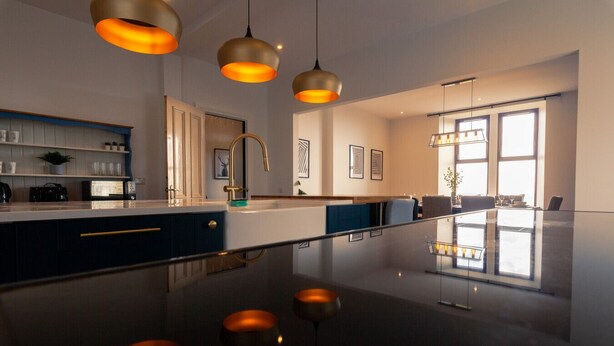 A modern kitchen with a central island, pendant lighting, and a dining area with a glass partition.