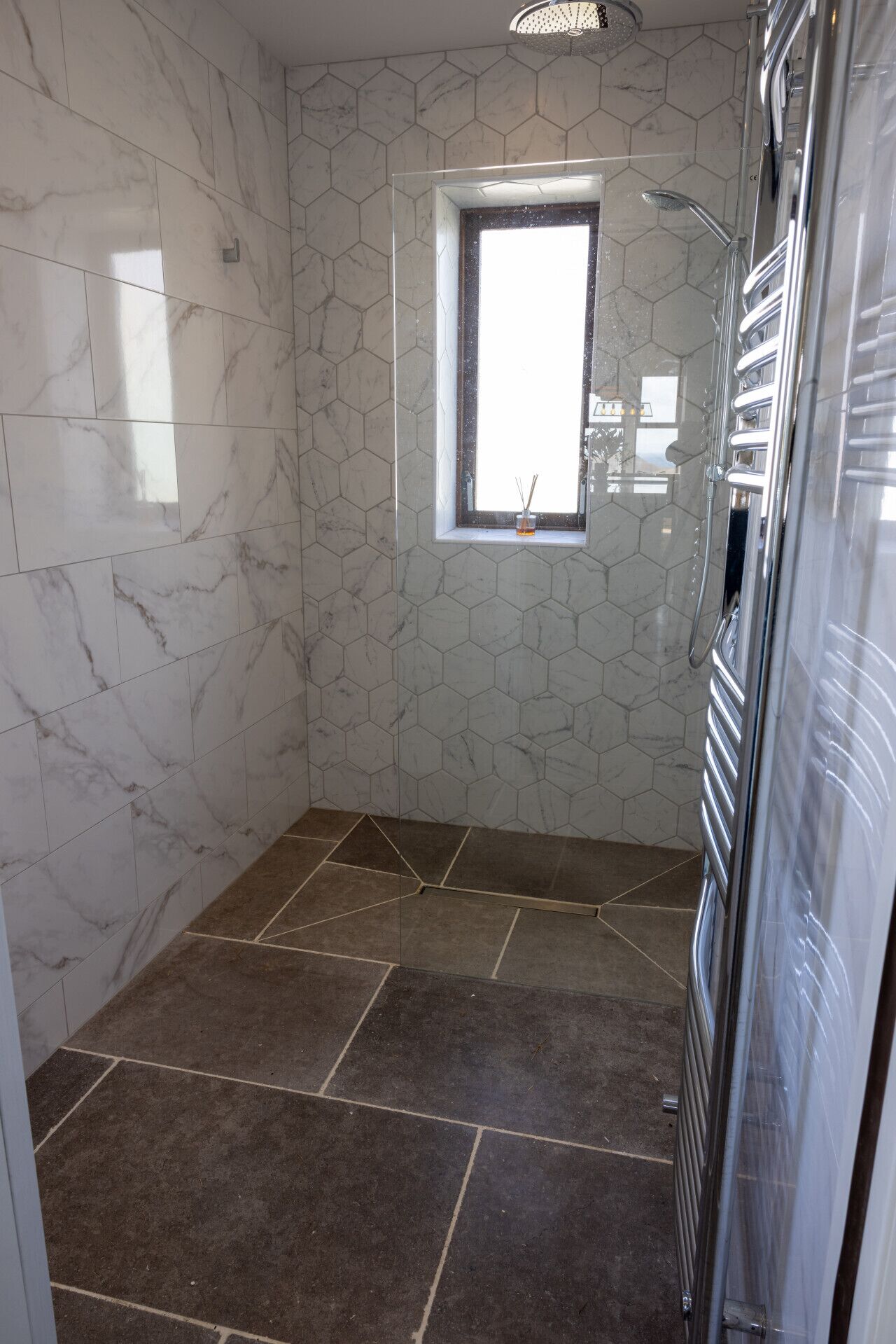 Une salle de bain avec des murs recouverts de carreaux hexagonaux, une fenêtre et un espace douche.