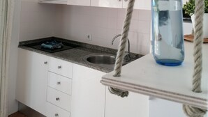 Une cuisine avec des meubles blancs, un plan de travail en granit, un évier en acier inoxydable et une plante suspendue dans un vase en verre bleu.