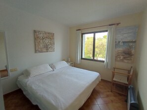 A bedroom with a bed, a window with curtains, a painting, and a chair.