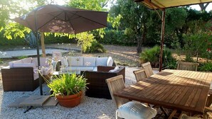 An outdoor patio area with a wooden table and chairs, a cushioned sofa, and a large umbrella providing shade. - Bright villa with pool in Grimaud (Grimaud)