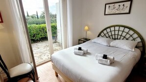 A hotel room with a bed, two bedside tables, a chair, and a view of a garden through a glass door. - Bright villa with pool in Grimaud (Grimaud)