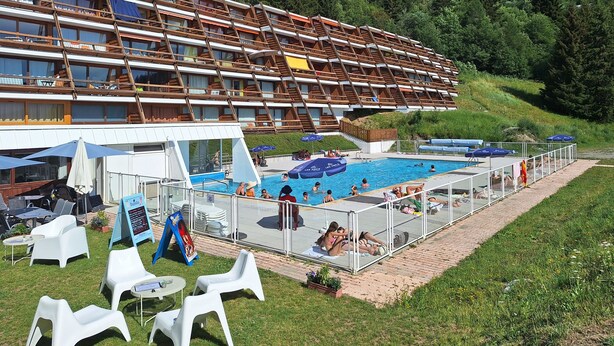 Hotel com piscina ao ar livre, espreguiçadeiras e vista para uma montanha.