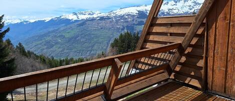 A wooden staircase leading to a balcony with a view of snow-capped mountains.
