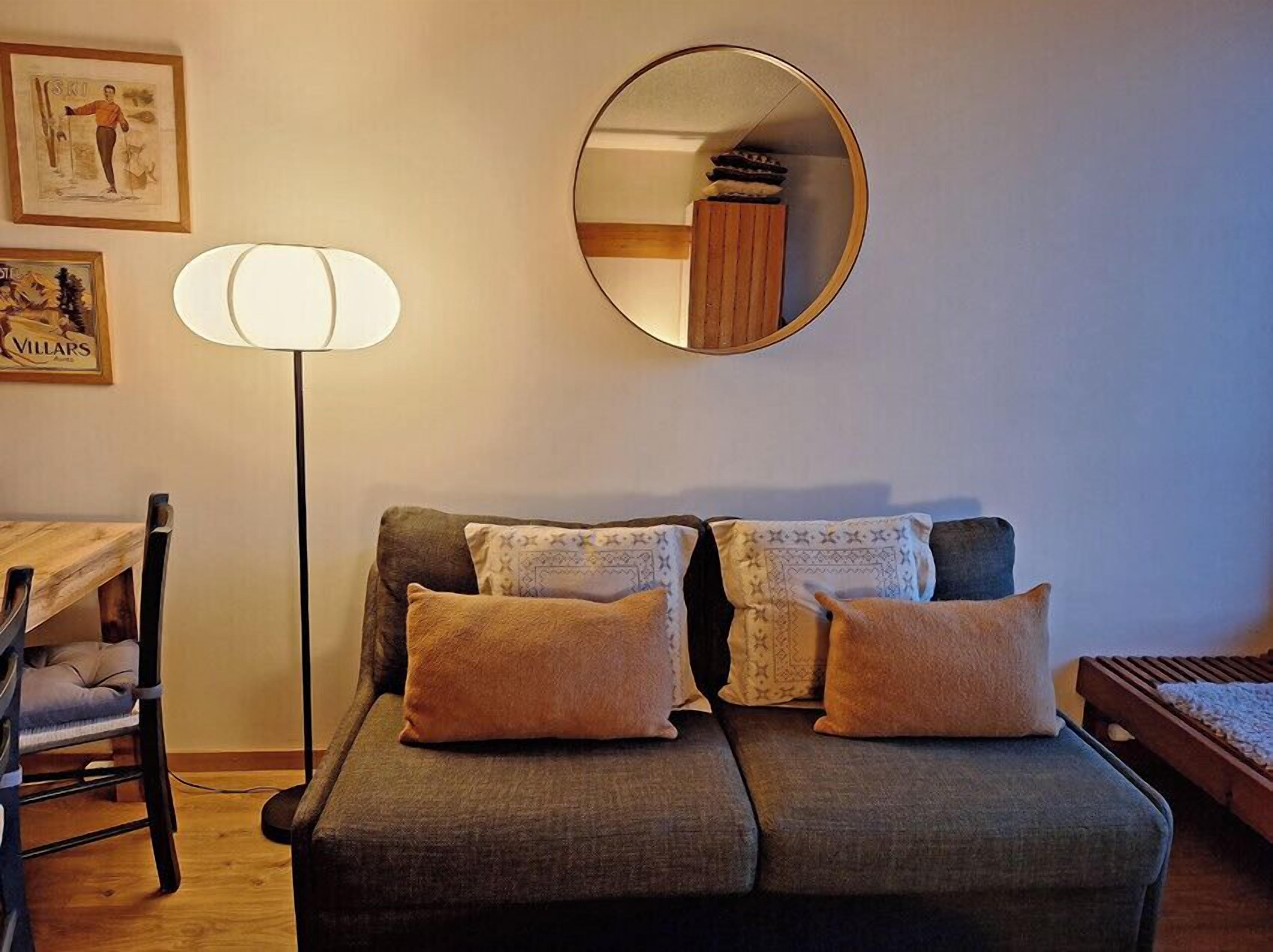 Un salon chaleureux avec un canapé, deux coussins, une lampe sur pied, un miroir et des tableaux encadrés accrochés au mur.