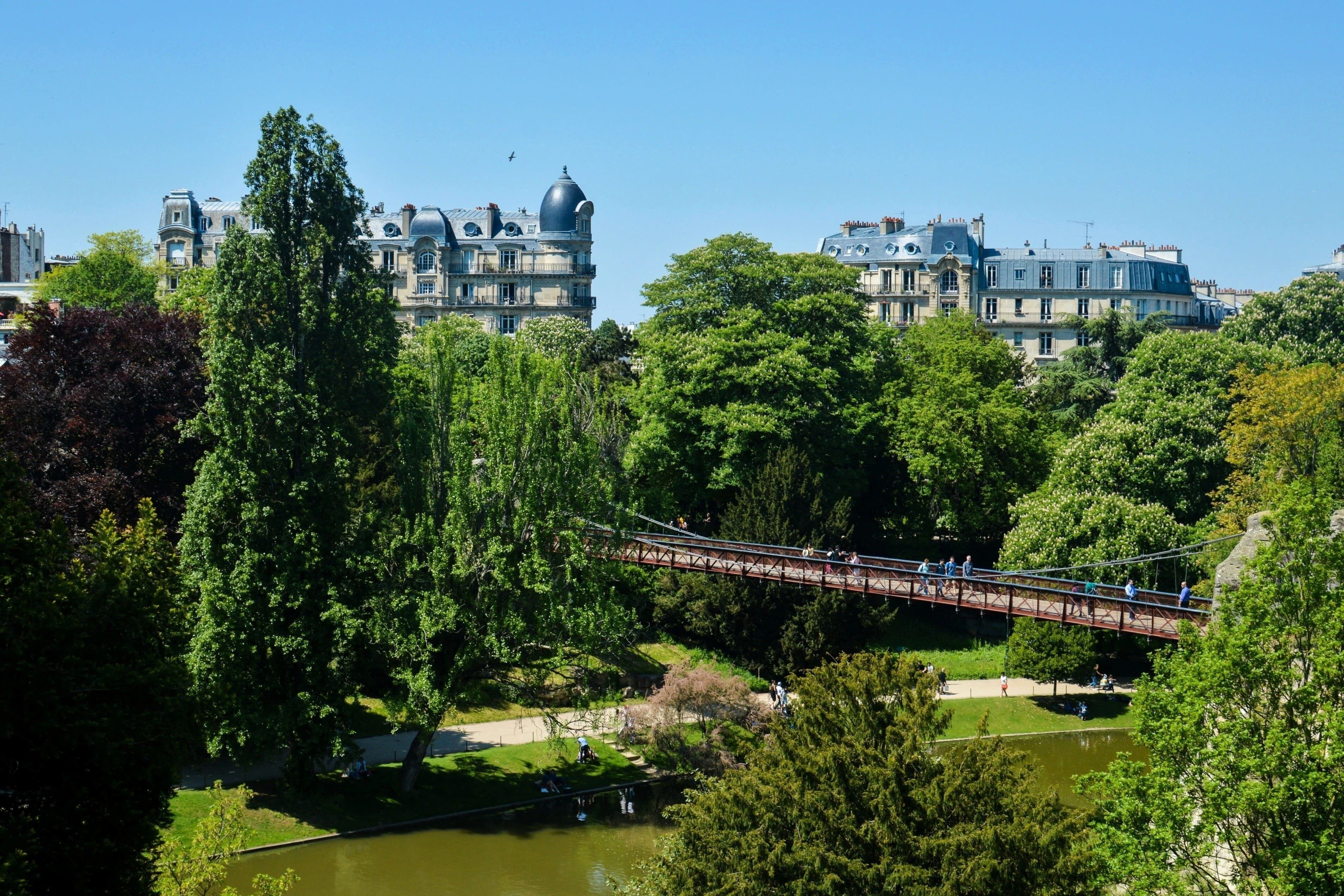 A park with a bridge, trees, and a body of water.