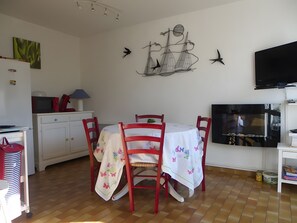 Un comedor con una mesa, sillas, una obra de arte en la pared, un televisor y una cocina con armarios y electrodomésticos.