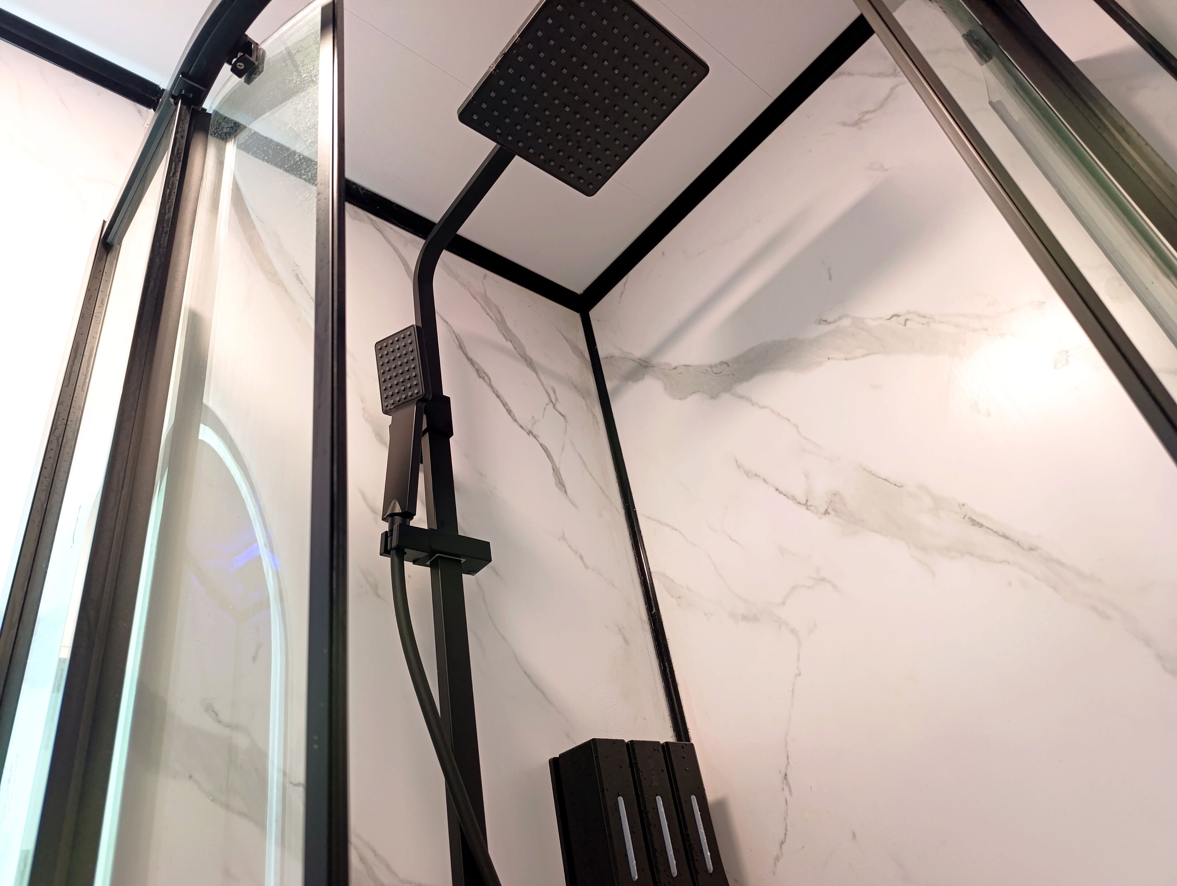 Une douche fermée par des parois en verre, dotée d’un pommeau de douche à main et d’un panneau fixe.