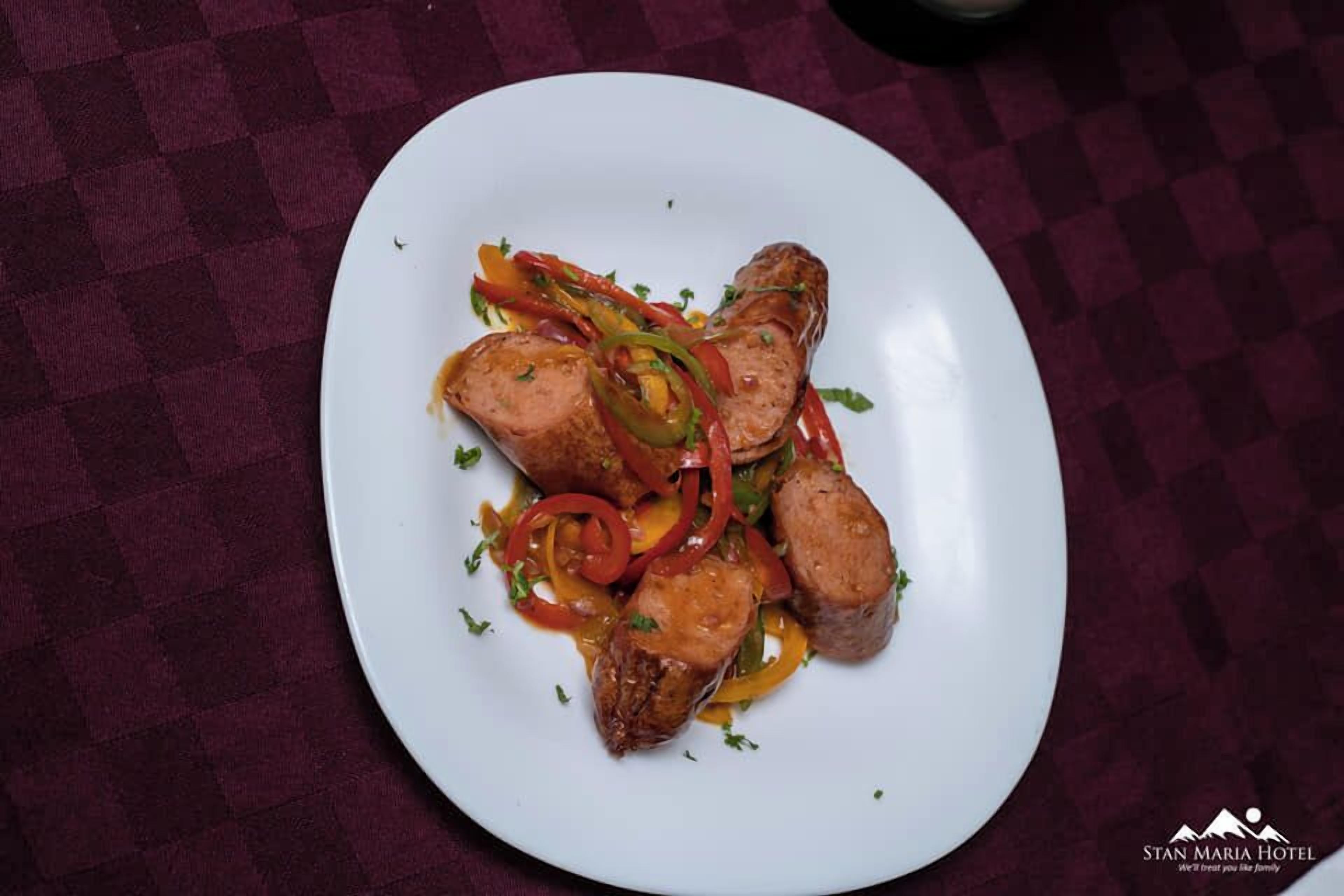 Ein weißer Teller mit Wurstscheiben und Paprika auf einer karierten Tischdecke.