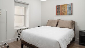 A bedroom with a bed, a window, a radiator, a wall-mounted artwork, and a nightstand.