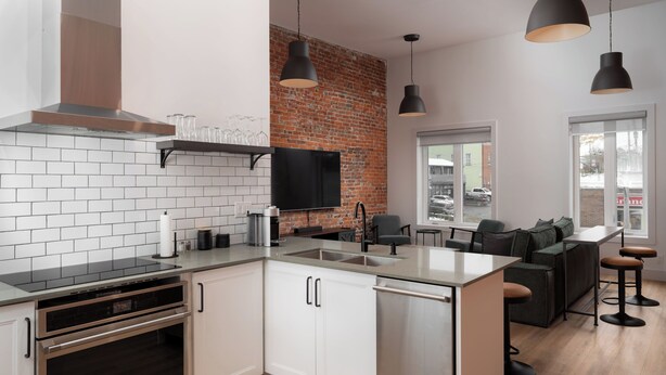 A modern kitchen with white cabinetry, a brick accent wall, a built-in oven, and a large island with bar stools.