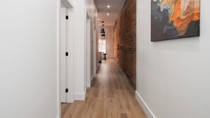 A hallway with wooden flooring, white walls, and a brick accent wall.