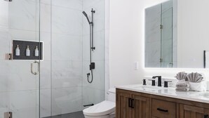 A modern bathroom with a glass-enclosed shower, a toilet, and a vanity with a mirror and towel rack.
