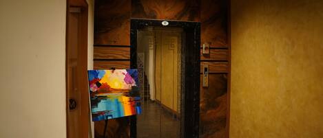 An elevator with a digital display showing the number 2, a wooden panel wall, and a colorful painting on the left.