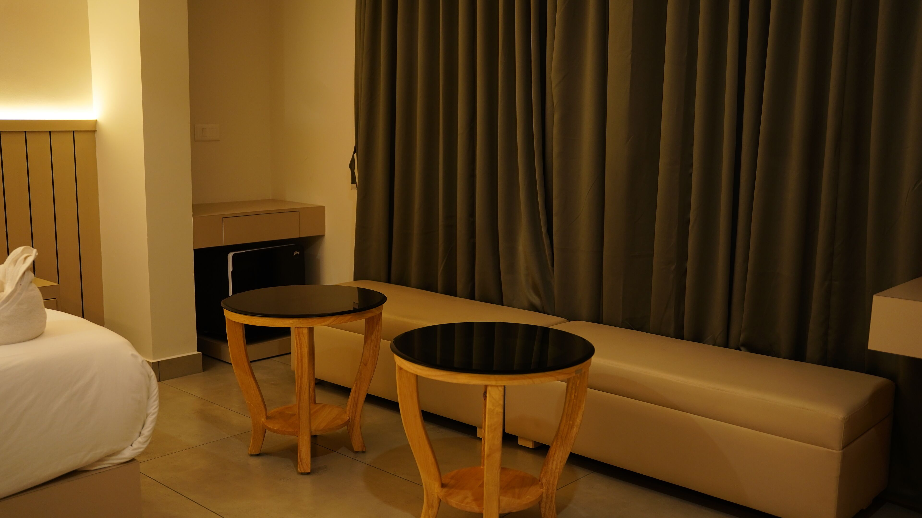Une chambre d’hôtel avec un lit, deux tables de chevet en bois, un canapé, une petite table avec une lampe et un rideau.