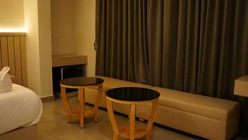 A hotel room with a bed, two wooden side tables, a sofa, a small table with a lamp, and a curtain.