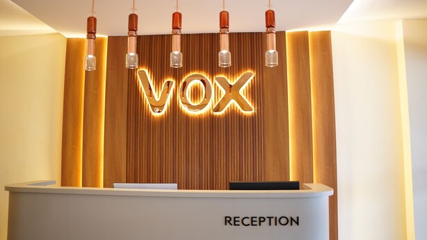 A reception desk with a wooden backdrop and illuminated 'VOX' letters. - Vox Holiday (Palakkad)
