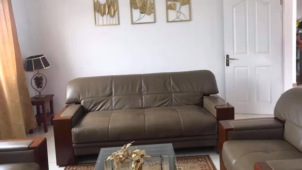 Una sala de estar con un sofá de cuero marrón, una mesa de centro de vidrio con objetos decorativos y tres obras de arte con hojas enmarcadas en la pared.