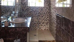Un baño moderno con un espejo grande, dos lavamanos, ducha y ventana con vistas a zonas verdes.