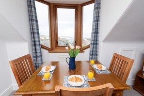 A dining table with four chairs, a vase with flowers, and plates with croissants and orange juice. - Stylish Lerwick 2BR Apt with Harbour & Town Views (Lerwick)