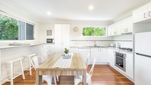 Een moderne keuken met witte kastjes, een houten eettafel en uitzicht op groen.