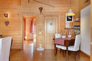 Een houten interieur met een eettafel, stoelen, een hanglamp en een deur met een bordje.