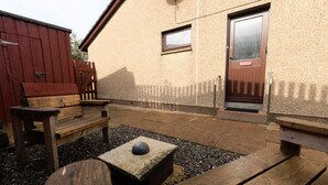 An outdoor patio area with wooden benches and a small table, a red shed, and a building with a door and window. - NEW to VRBO: Peaceful Lerwick Stay; Large Garden, Isles Views (Lerwick)