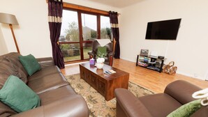 A living room with leather sofas, a coffee table, a TV, and a window with curtains. - NEW to VRBO: Peaceful Lerwick Stay; Large Garden, Isles Views (Lerwick)