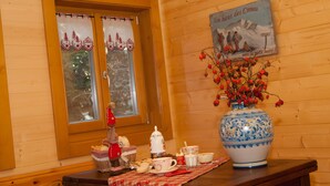 Interior de una cabaña de madera con una mesa servida para tomar té, un florero con bayas rojas y un cartel en la pared.