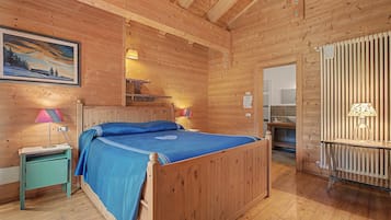 Una habitació de fusta amb un llit, una tauleta de nit, una làmpada i un quadre a la paret.