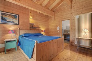 Een kamer met houten vloeren, een bed, een nachtkastje, een lamp en een schilderij aan de muur.