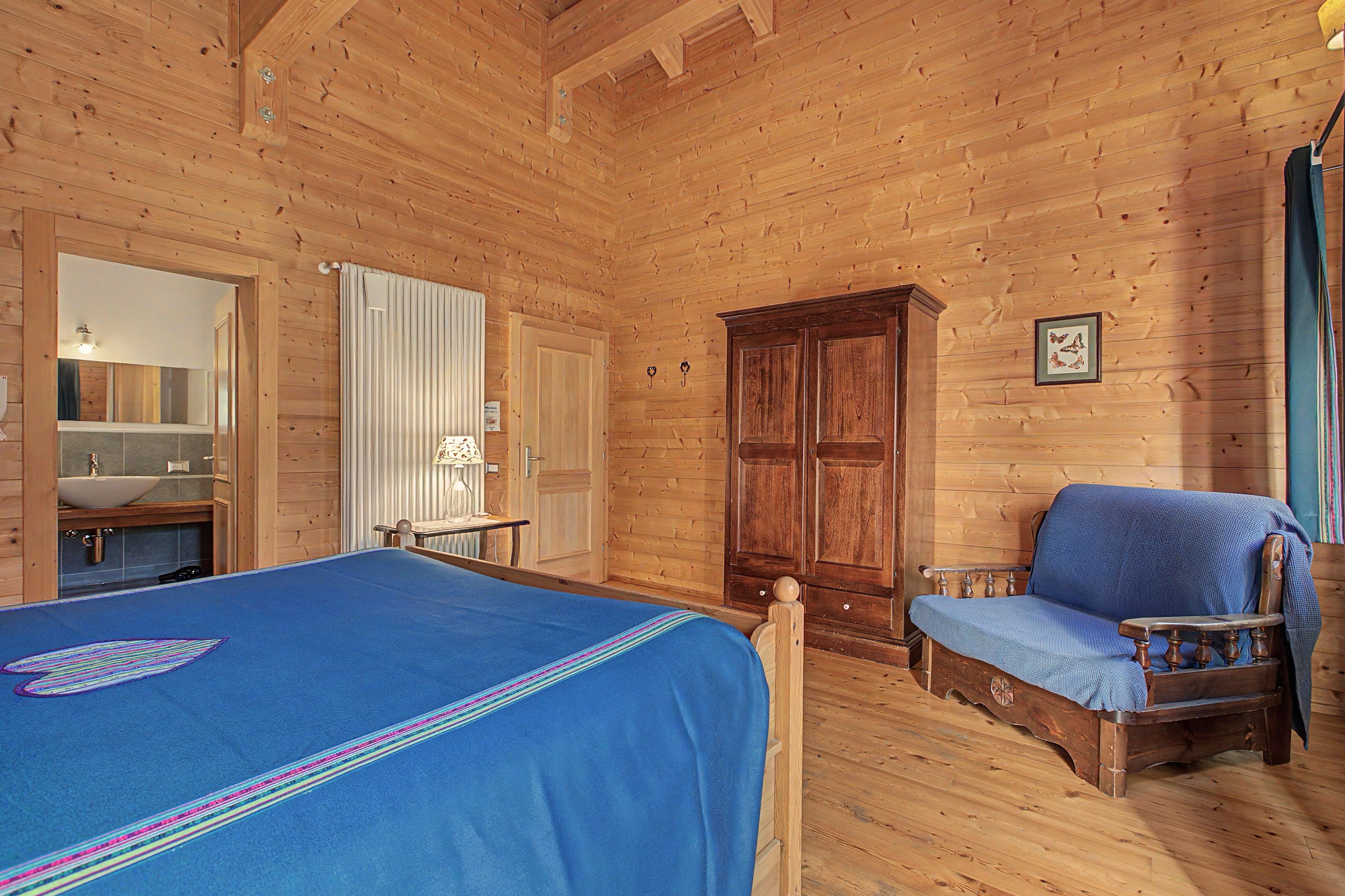 A wooden cabin room with a bed, a chair, a wardrobe, and a mirror.