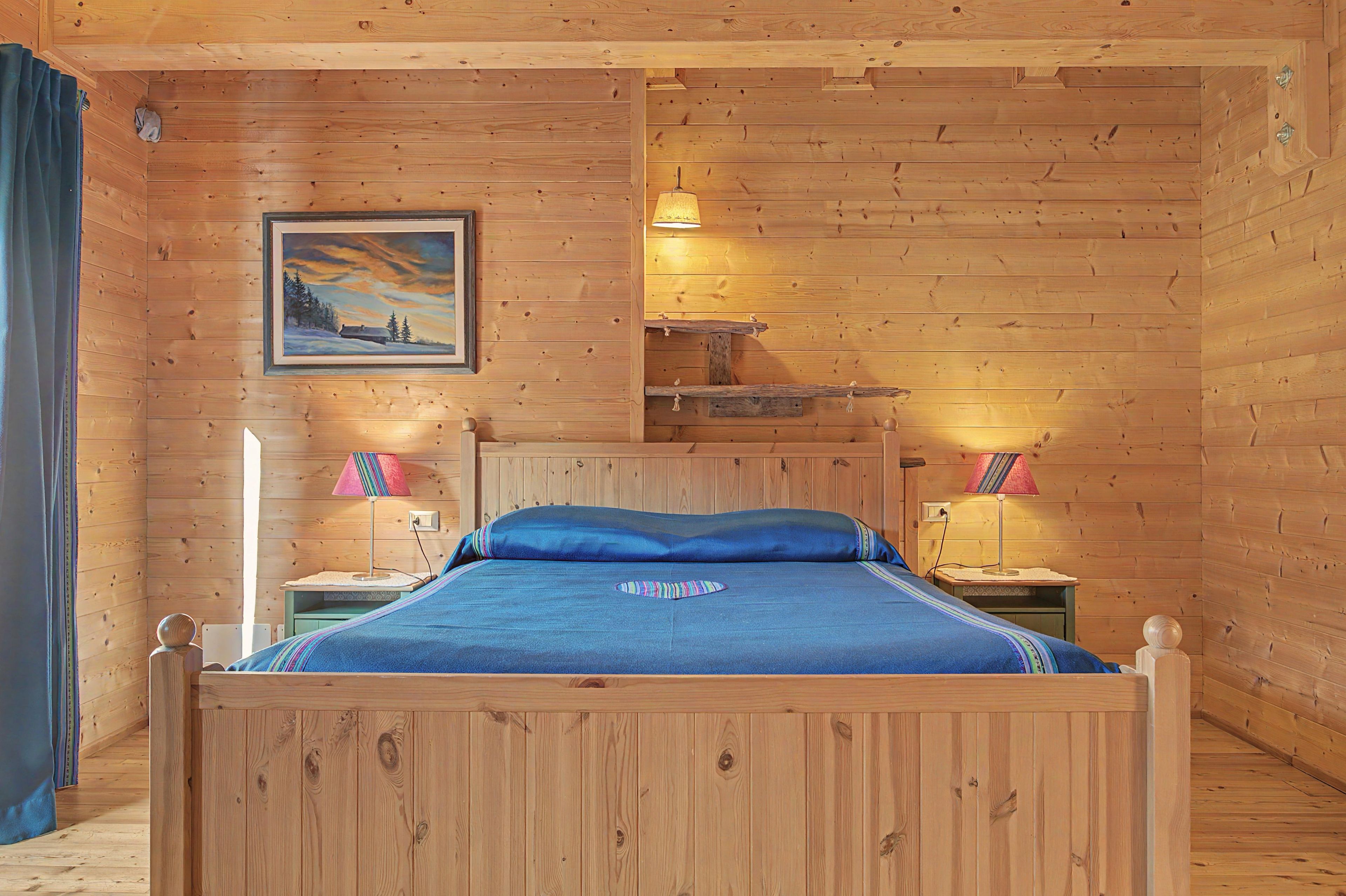 Ein Zimmer mit Holzboden, einem Bett, zwei Nachttischlampen, einem Bild und einem Regal.